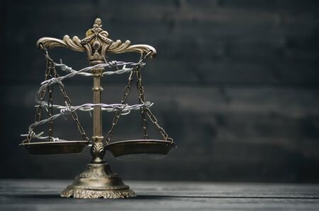 Scales of Justice and barbed wire on a black wooden background, Compromised Rule of Law, Weakness of...
