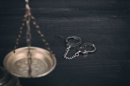 Law and Justice, Legality concept, Scales of Justice and handcuffs on a black wooden background.