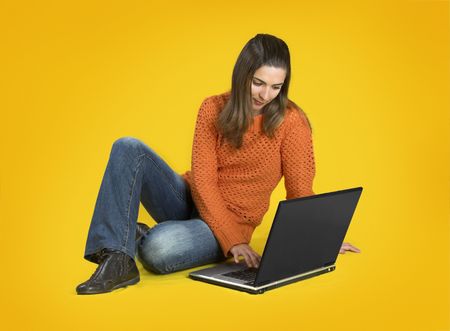 Beautiful student woman with a laptop over a yellow backgroundの写真素材