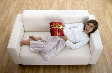 Woman in pajama seated on a sofa holding a Christmas giftの写真素材