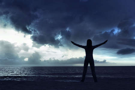 Woman silhouette relaxing on the beach at the sunsetの写真素材