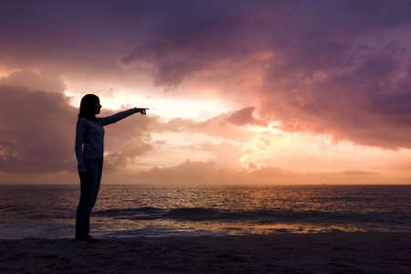Woman silhouette relaxing on the beach and looking to the sunsetの写真素材