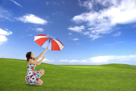 Portrait of a young and happy woman posing with a umbrella on a beautiful green fieldの写真素材