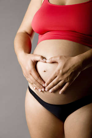 Pregnant women wrap her arms around the belly in the form of the heart. Isolated on white. 