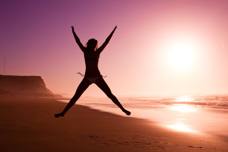 Picture of a female silhouette of a young girl jumping on the beach at the sunsetの写真素材