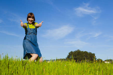 Portrait of a beautiful woman on a green meadow with thumbs upの写真素材
