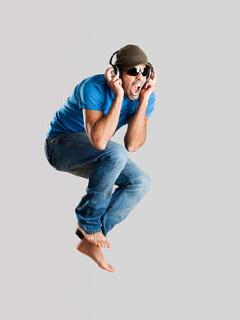 Young man jumping and listening music isolated over a gray background