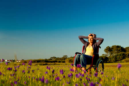 Handicapped woman on a wheelchair over a green meadowの写真素材