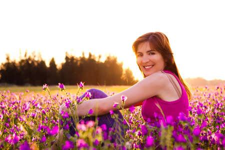 Beautiful young woman sitting on a flowery meadowの写真素材
