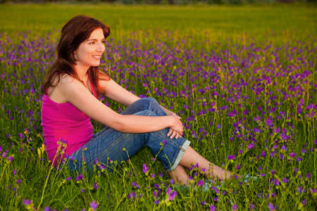 Beautiful young woman sitting on a flowery meadowの写真素材