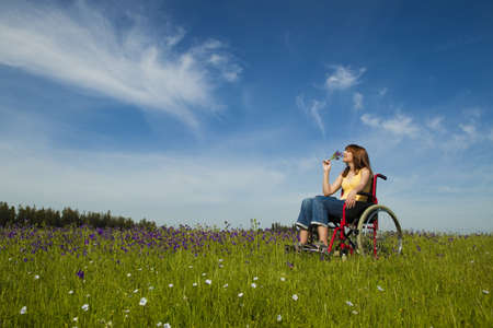 Happy handicapped woman on a wheelchair over a green meadow の写真素材