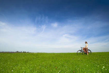 Happy young woman with a vintage bicycle on a green meadowの写真素材