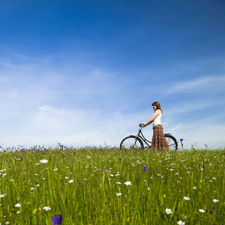 Happy young woman with a vintage bicycle on a green meadowの写真素材
