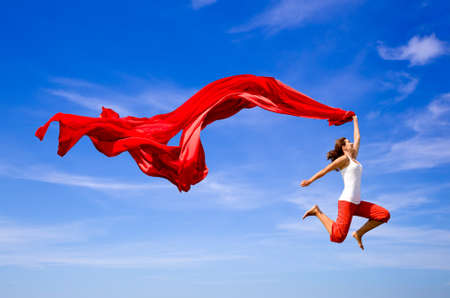 Beautiful young woman jumping over the blue sky with a colored tissueの写真素材