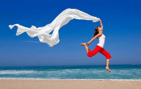 Beautiful young woman jumping on  the beach with a colored tissueの写真素材