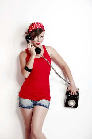 Beautiful and fashion young woman with a pin-up look. posing with a vintage phoneの写真素材