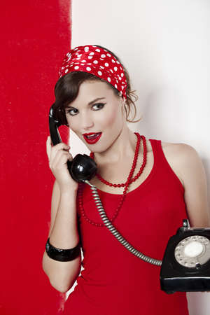 Beautiful and fashion young woman with a pin-up look. posing with a vintage phoneの写真素材