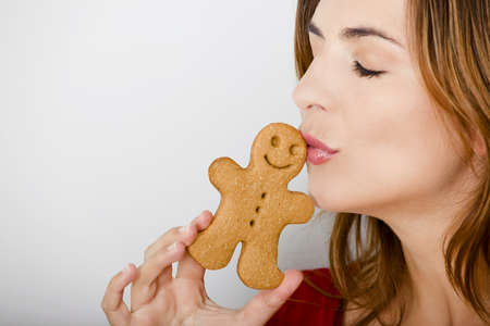 Beautiful young woman kissing a gingerbread man cookieの写真素材
