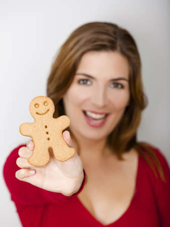 Beautiful young woman holding a gingerbread cookie, focus is on the ginger manの写真素材