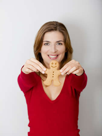 Beautiful young woman holding a gingerbread cookie, focus is on the ginger manの写真素材