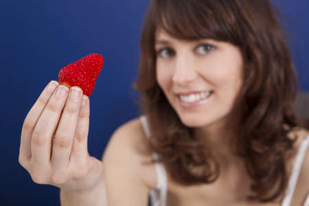 Beautiful young woman holding and showing a big and fresh strawberry