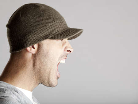 Profile portrait of a young man yelling, isolated on a gray background