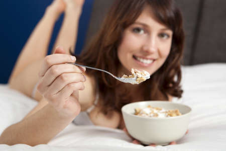 Beautiful and healthy young woman eating a cup of cereals with yogurtの写真素材