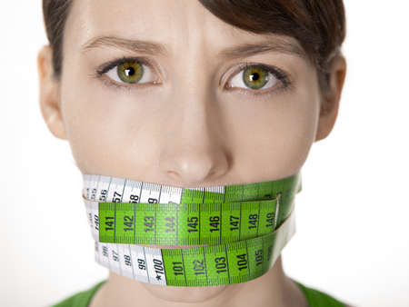 Portrait of a young  woman with a green measuring tape covering the mouthの写真素材