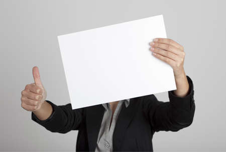 Woman showing a blank paper sheet in front of her head and making a thumbs up gesture with the right hand
の写真素材