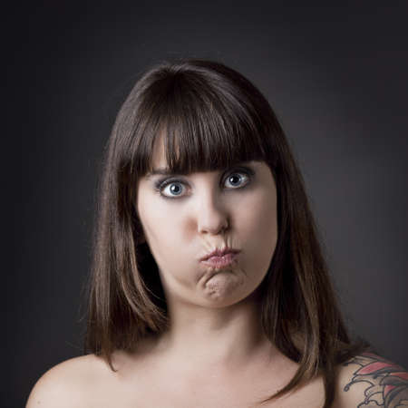 Portrait of a beautiful and funny woman with cheeks full of air against a grey background