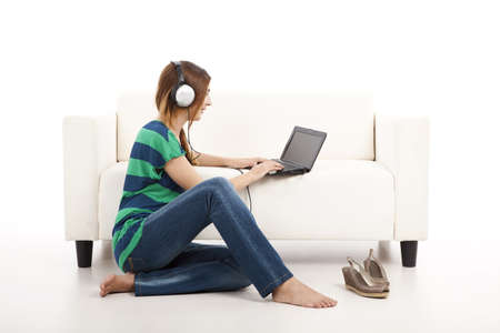 Beautiful young woman using a laptop and listen music, isolated on whiteの写真素材