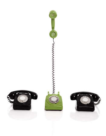 Green phone ringing in the midle of two black phones, isolated on white backgroundの写真素材