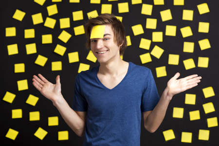 Happy student with a reminder on the head, and with more yellow paper notes in the background