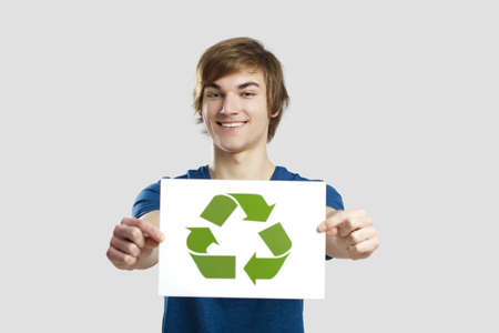 Casual young man holding a recycling sign to promote a green and better world, over a gray backgroundの写真素材