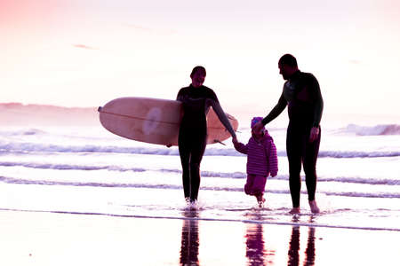 Female surfer and her familly walking in the beach at the sunsetの写真素材