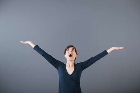 Portrait of a successful young woman with arms up over a grey backgroundの写真素材
