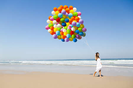 Beautiful girl walking in the beach holding dozens of colored balloons