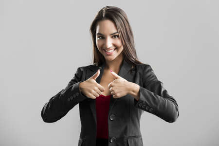 Beautiful business woman with thumbs up, over a gray background