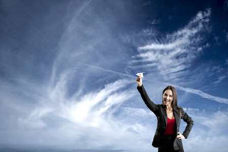 Beautiful business woman throwing a paper plane, against a beautiful blue skyの写真素材