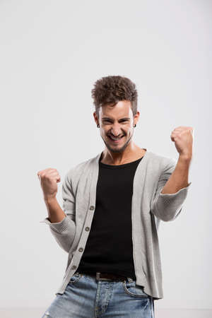 Happy young man with arms up, over a gray backgroundの写真素材