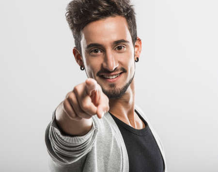 Handsome young man looking and pointing to the camera, over a gray background
