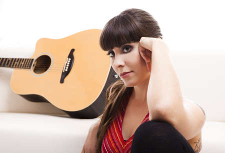 Beautiful woman sitting Ã­n the floor  with her guitar, isolated on whiteの写真素材