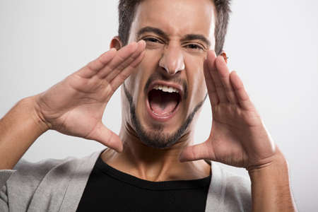 Portrait of a handsome young man yelling, over a gray background