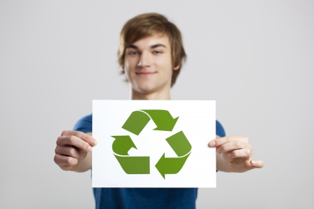 Casual young man holding a recycling sign to promote a green and better world, over a gray backgroundの写真素材