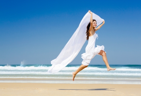 Beautiful woman running and jumping in the beach with a white tissueの写真素材
