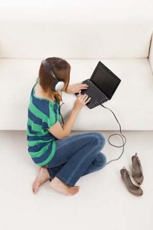 Beautiful young woman using a laptop and listen music, isolated on whiteの写真素材