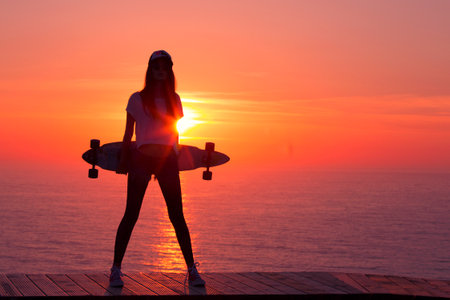 Beautiful and fashion young woman posing at teh sunset with a skateboard