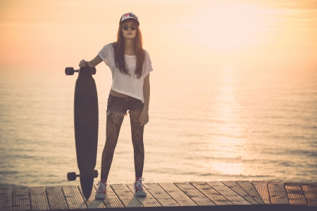 Beautiful and fashion young woman posing at teh sunset with a skateboard - File a little bit noisy