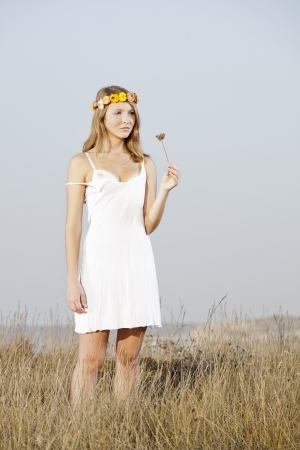 Beautiful young woman in a meadow holding a flowerの写真素材