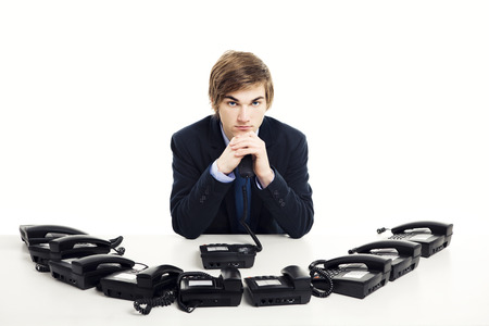 Businessman sitting with a bunch telephones on his front